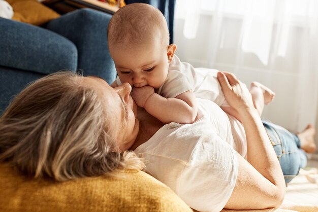 A cute joyful baby and his grandmother are lying on the floor in a bright cozy room happy childhood