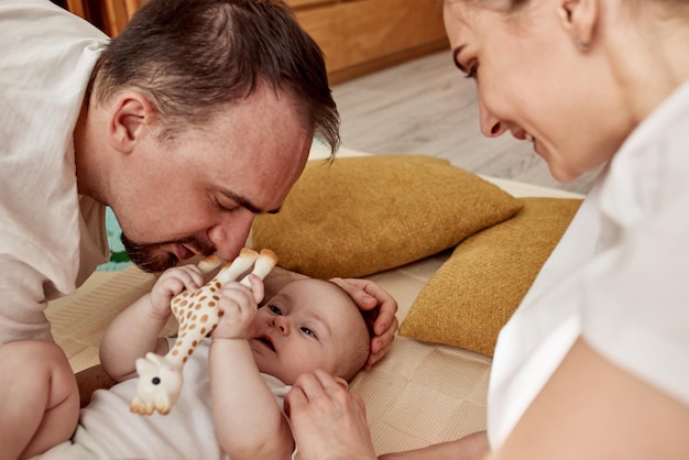 A cute joyful baby and his parents lie on the floor in a bright cozy room with toys mom and dad hug