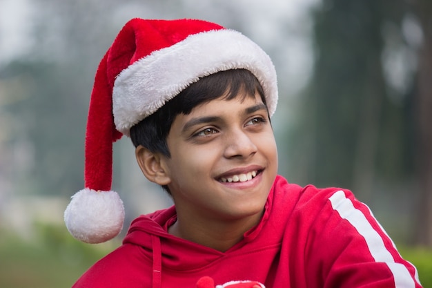 A cute joyful boy with Santa cap and red tshirt smiling happily and looking at a distance