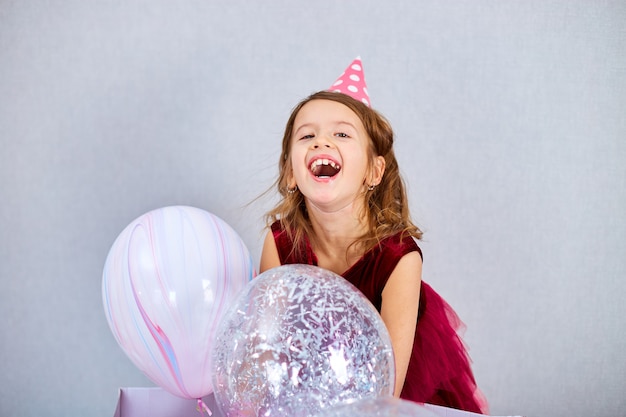 Cute, Joyful little girl in pink dress and hat play with balloons at home birthday party streamers, Happy birthday. Celebrating