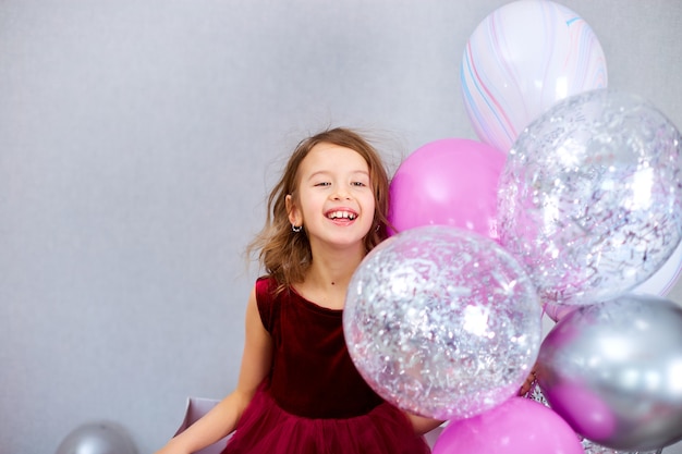 Cute Joyful little girl in pink dress and hat play with balloons at home birthday party streamers