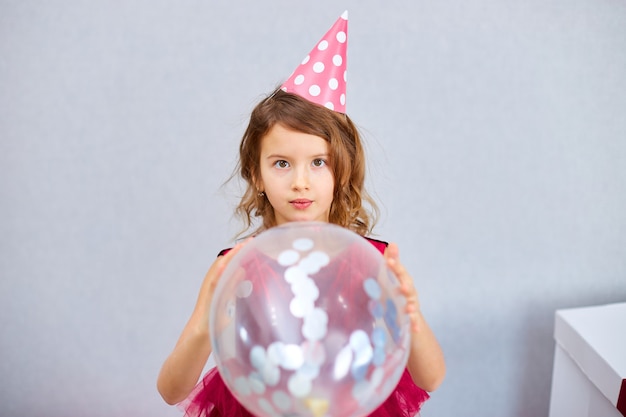 Cute, Joyful little girl in pink dress and hat play with balloons at home birthday party