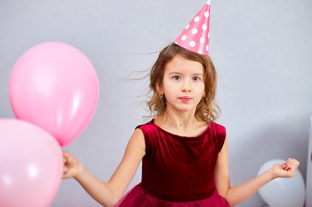 Cute, Joyful little girl in pink dress and hat play with balloons at home birthday party