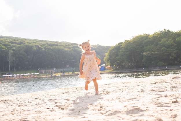 Cute kid girl in dress with funny tails running on sand on sunny summer day