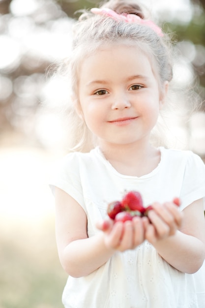 Cute kid girl eating strawberries outdoors