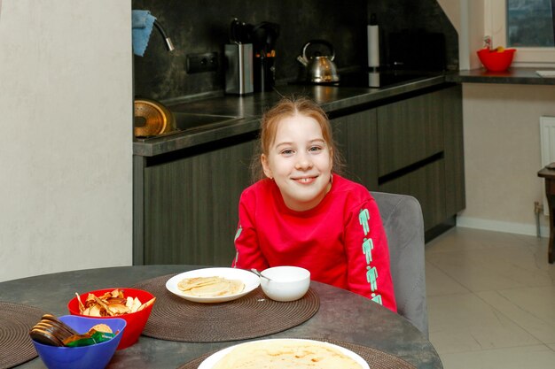 cute kid girl at home at the table in front of a plate of pancakes