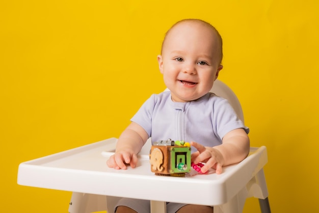 A cute kid is sitting in a child39s chair playing with an educational wooden toy on a yellow background biziboard