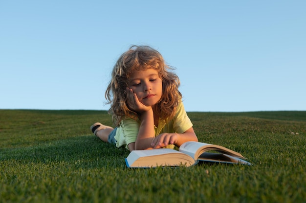 Cute kid reading book on green grass schoolboy with a book having a rest outdoor