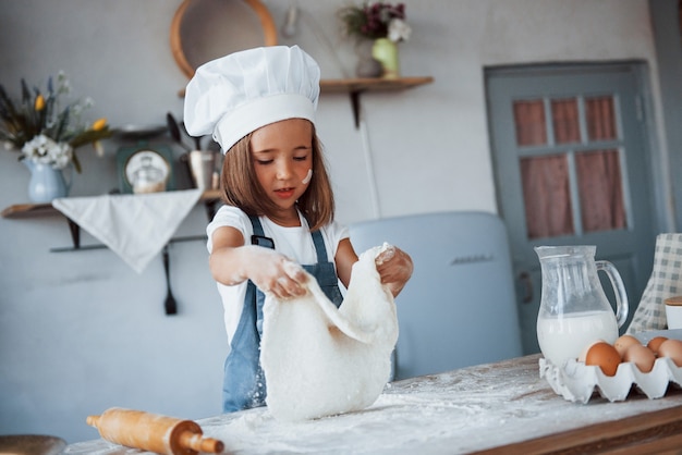 Cute kid in white chef uniform preparing food on the kitchen.