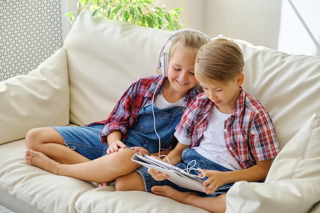 Cute kids with headphones enjoying tablet at home