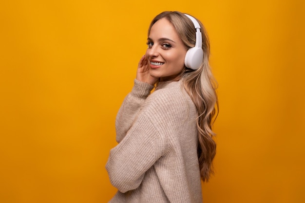 Cute lady joyfully listens to music with big headphones on orange background