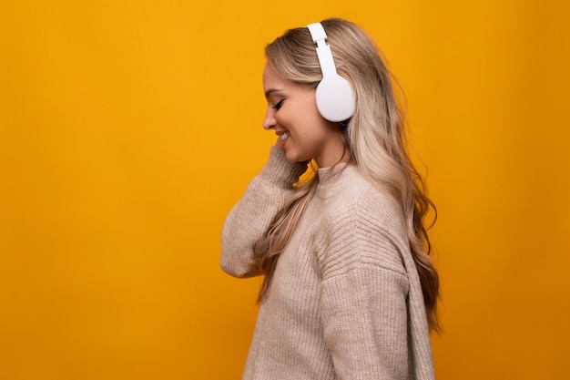 Cute lady joyfully listens to music with big headphones on orange background