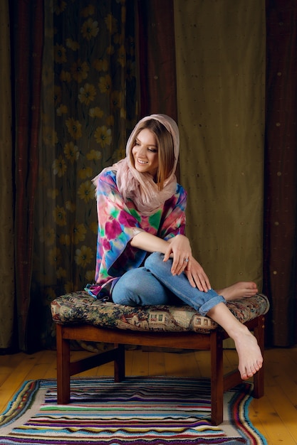 Cute lady in silk scarf around her head posing on sofa with colorful fabric