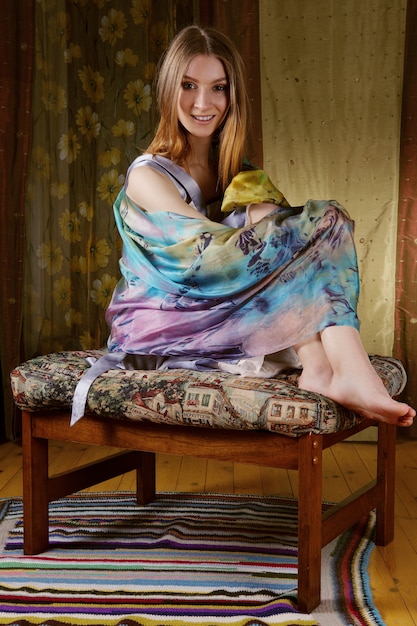 Cute lady in silk scarf around her head posing on sofa with colorful fabric