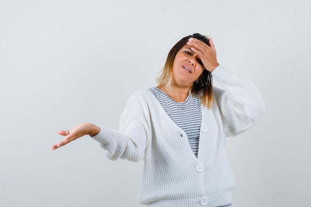 Cute lady in t-shirt, cardigan holding hand on forehead, spreading palm aside and looking wistful