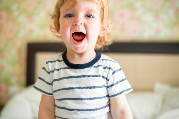 Cute laughing child boy sits in bed boy plays at home child in a sunny bedroom