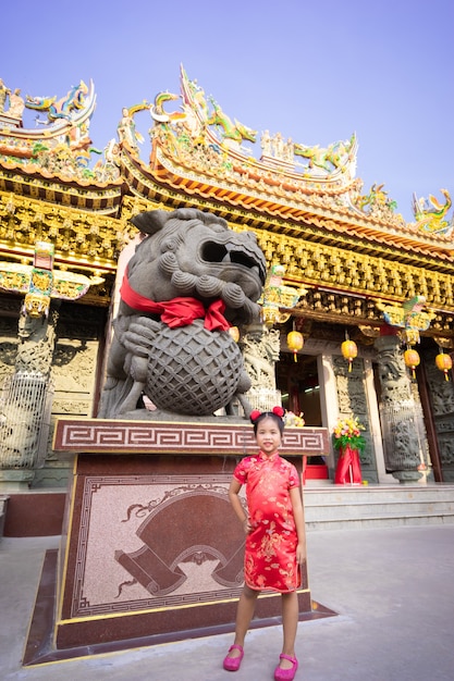 Cute little asian girl in chinese traditional dress smiling and standing near statue. Happy chinese new year concept.