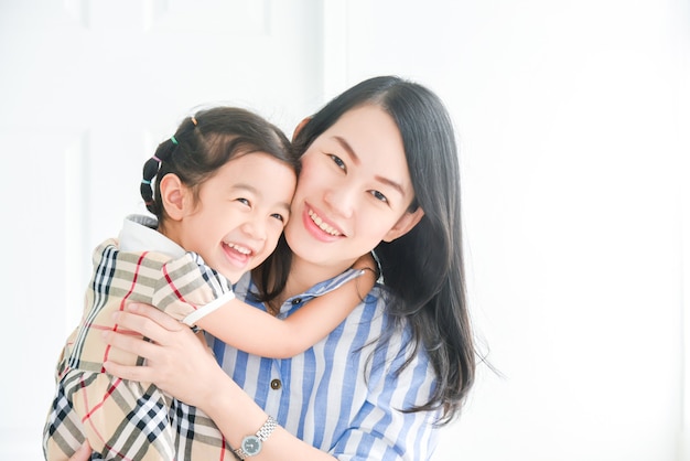 Cute little asian girl hugging her mom show love and affection, smiling mother and small daughter having fun at home embrace sharing close tender moment together.