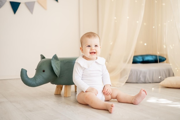 Cute little baby boy or girl in a bright children's room with a wigwam and an elephant in a white cotton bodysuit playing