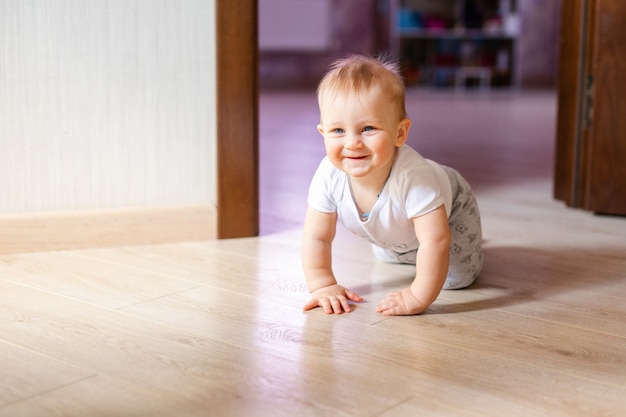 Cute little baby boy lying on hardwood and smiling. Child crawling over wooden parquet and looking up with happy face. View from above. Copyspace.