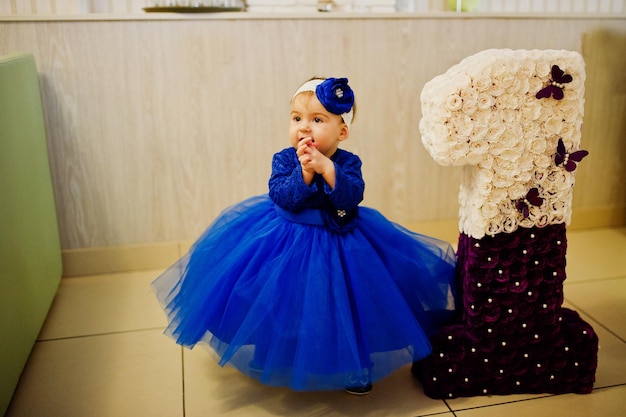 Cute little baby girl at blue dress near 1 year birthday number