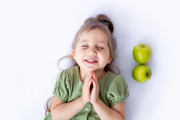 A cute little baby girl is holding a big green apple in her hands White isolated background Healthy foods for children or a healthy snack Space for text Highquality photography