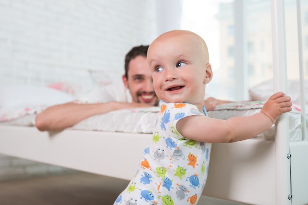 Cute little baby is standing on the edge of bed