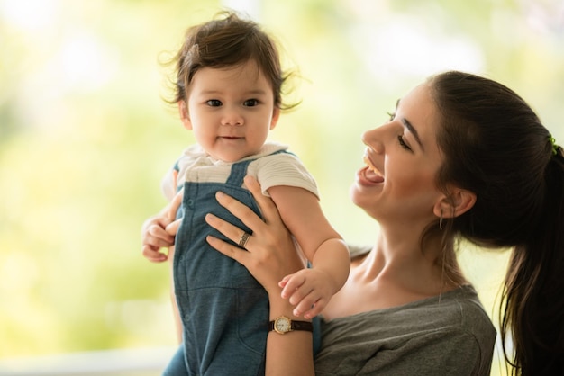 Cute little baby toddler playing and enjoying while in the arms of young mother hugging at home