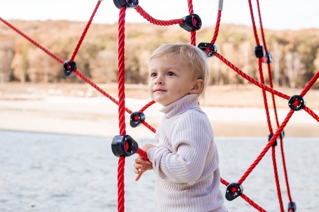 Cute little blonde boy in knitted sweater plays in the childrens town in the city park in the fall