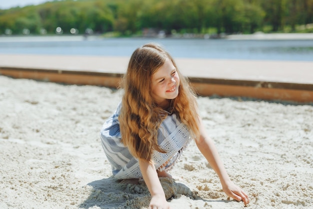 Cute little blonde girl playing in the sand on the beach summer