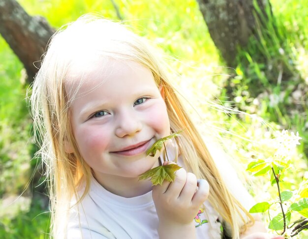 Cute little blonde girl with a branch of blooming bird cherry tree on the meadow in spring park