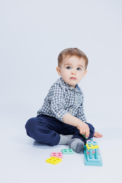 A cute little boy in a checkered shirt sits on a white background and plays with wooden educational toys Ecological wooden toys for children