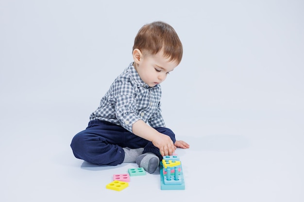 A cute little boy in a checkered shirt sits on a white background and plays with wooden educational toys Ecological wooden toys for children