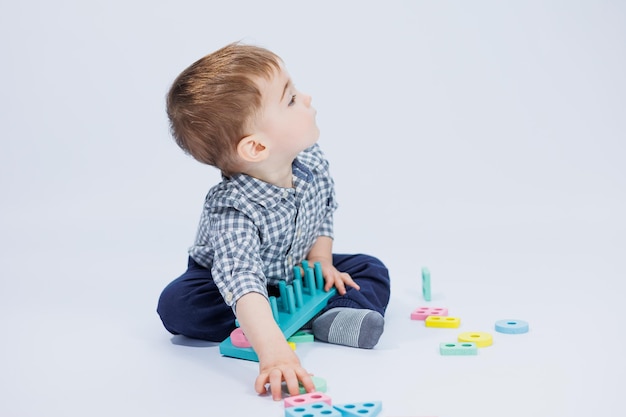 A cute little boy in a checkered shirt sits on a white background and plays with wooden educational toys Ecological wooden toys for children