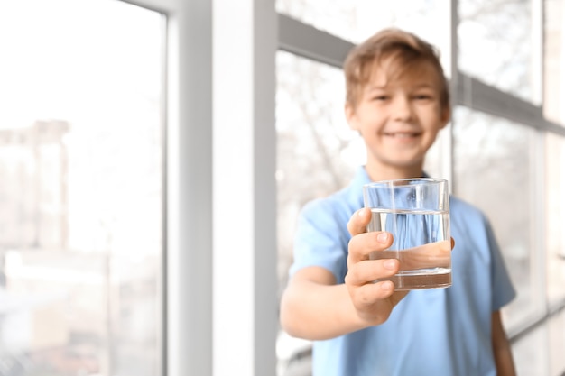 Cute little boy drinking water near window