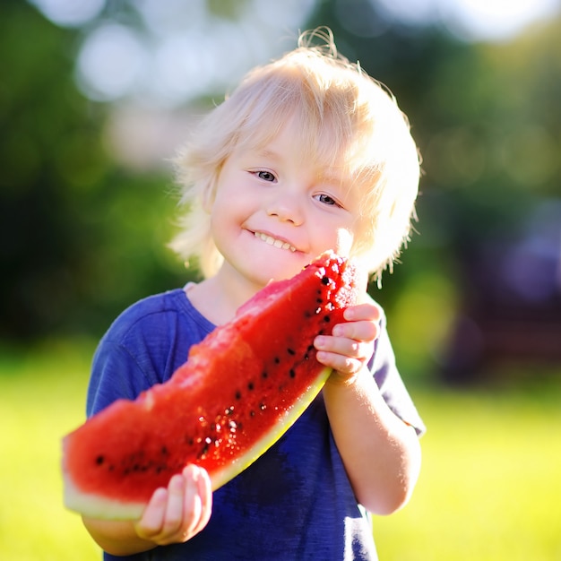 Cute little boy eating fresh watermelon outdoors