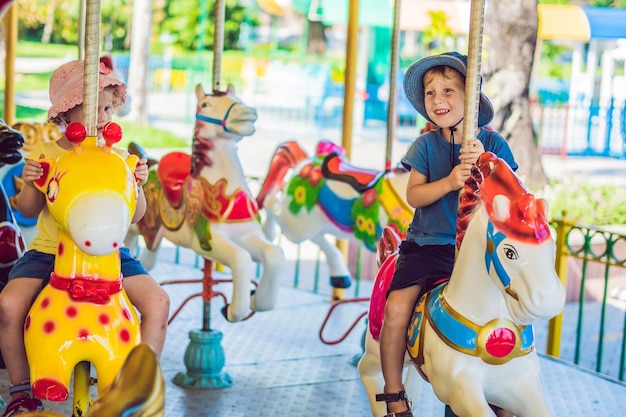 Cute little boy and girl enjoying in funfair and riding on colorful carousel house.