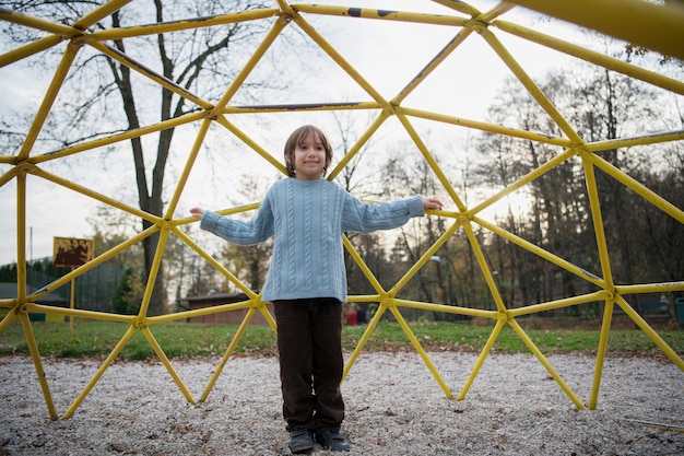 cute little boy having fun in playground park on cludy autum day