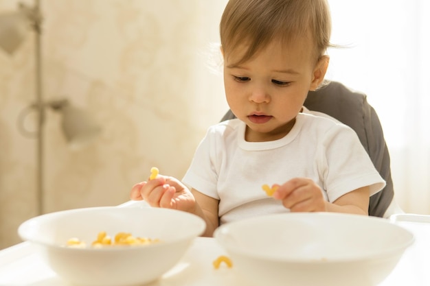 Cute little boy on a high chair playing with pasta