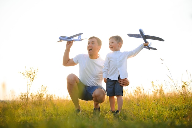 Cute little boy and his handsome young dad are smiling while playing with a toy airplane in the park