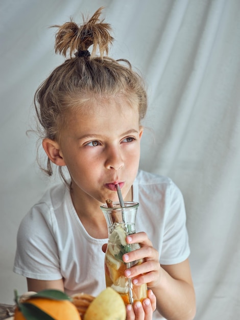 Cute little boy holding glass bottle with fresh cold beverage and drinking with metal straw while looking away