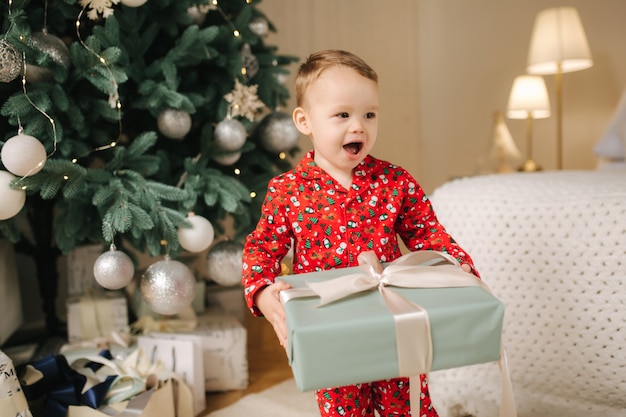 Cute little boy at home by the big Christmas tree looking for presents. Happy kid spend time on Holiday and enjoying every moment. Home alone.