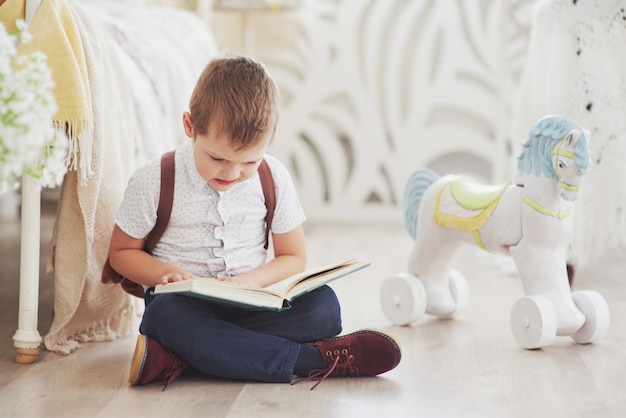 Cute little boy is going to school for the first time. Child with school bag and book. Kid makes a briefcase, child room