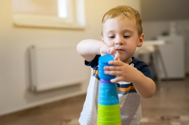 A cute little boy is playing with a multicolored pyramid indoors Toddler one and a half two years Selective focus