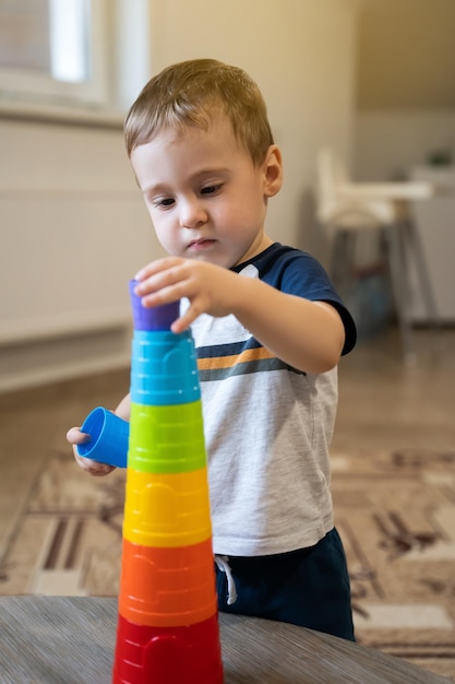 A cute little boy is playing with a multicolored pyramid indoors Toddler one and a half two years Selective focus