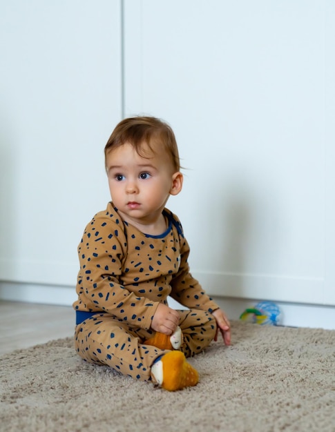 Cute little boy is playing with toys while sitting on floor Curious baby boy studying nursery room