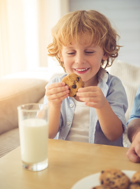 Cute little boy is smiling, drinking milk and eating cookies