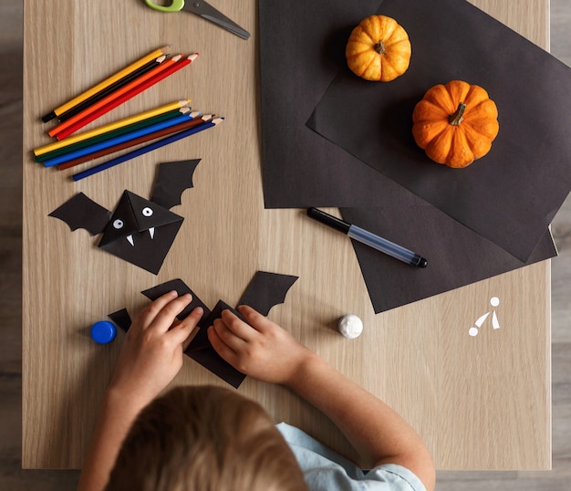 A cute little boy made a Halloween bat out of black paper. Children's handwork.