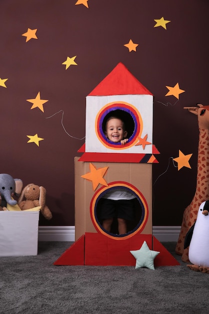 Cute little boy playing with cardboard rocket and toys at home Child's room interior