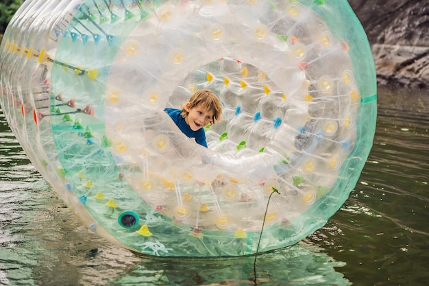 Cute little boy playing in Zorb a rolling plastic cylinder ring with a hole in the middle on the lake